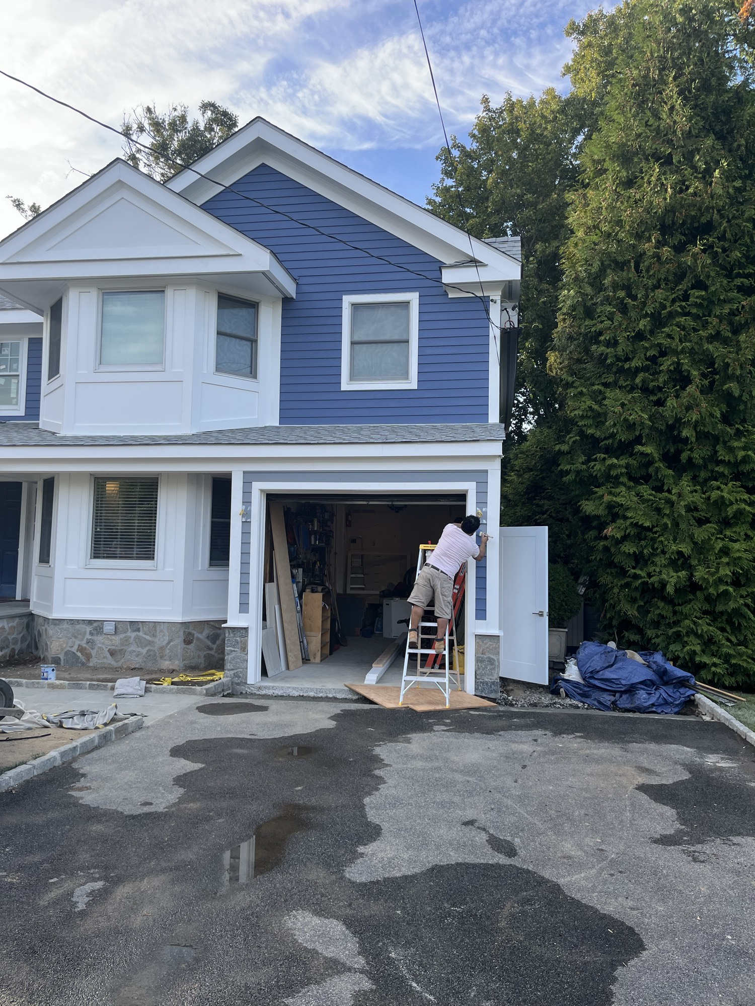 Painter finishing trim above the garage on blue siding